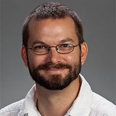 A color headshot of Andrew Kania smiling with full beard