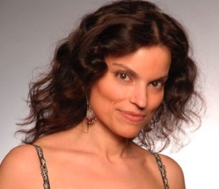 A color photographic cutout of Robert Gambarini from the shoulders up facing to the right wearing a gown with straps and red and white jewelry earrings.