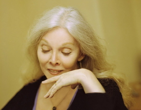 A glowing Jessica Williams with head turn down facing left with yellow background.