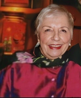 A color photograph of Carol Sloan with close cropped white hair wearing a red blouse late in her career.