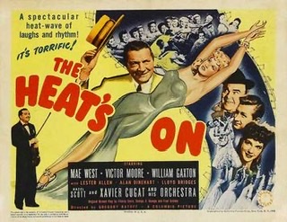 A color photograph of the movie poster for "The Heat's On" starring Mae West on the poster laying down in an evening dress at a diagonal from upper right corner to lower left surrounded by other cast members on a yellow background.