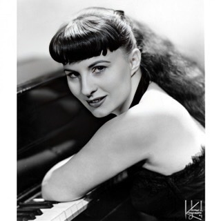 Jutta Hipp facing left with elbow resting on piano.