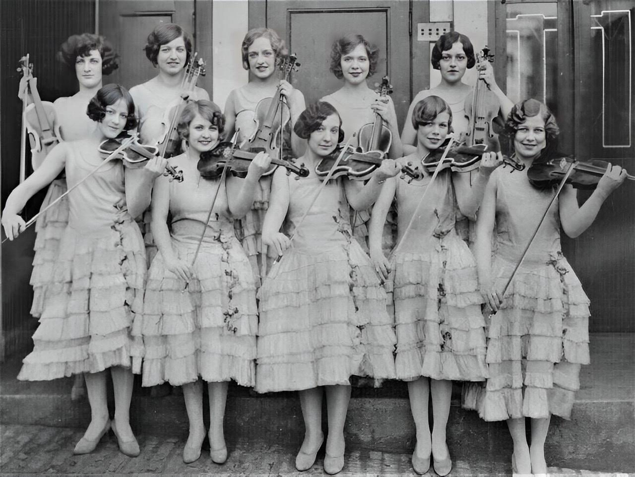 An enhanced black and white photograph of ten of The Ingenues each holding a violin.