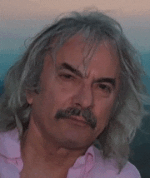 A color animated .gif of a headshot of Enrico Rava with flowing shoulder-length gray hair smiling and lifting up his eyebrows.