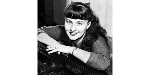 Jutta Hipp leaning on top of piano with both elbows.