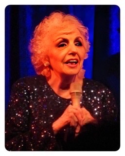 A color photograph of an older Carol Sloane holding a microphone.