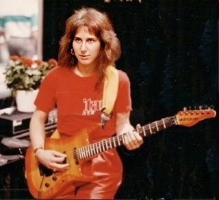 Emily Remler in an orange shirt playing her electric guitar.