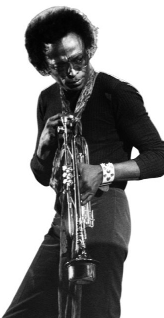 Miles Davis in a blue jean suit blowing his trumpet into a microphone stand probably around early 1970s.