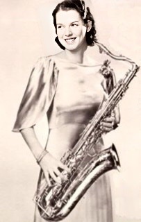A photograph of L'ana Hyams wearing a full length shiny silk dress standing in profile facing viewer's right holding a saxophone.