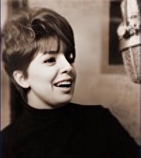 A color photograph of Carol Sloan in her twenties wearing a dark jersey at a microphone.