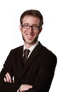 An enhanced photographic cutout of a smiling Martin Lücke with mutton chop sideburns and glasses in a black jacket.