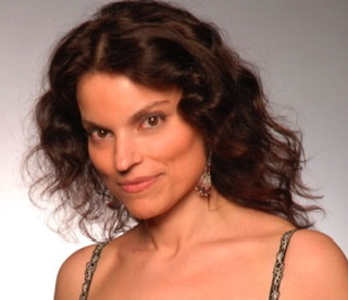 A color photographic cutout of Robert Gambarini from the shoulders up facing to the left wearing a gown with straps and red and white jewelry earrings.