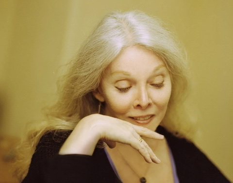 A glowing Jessica Williams with head turn down facing left with yellow background.