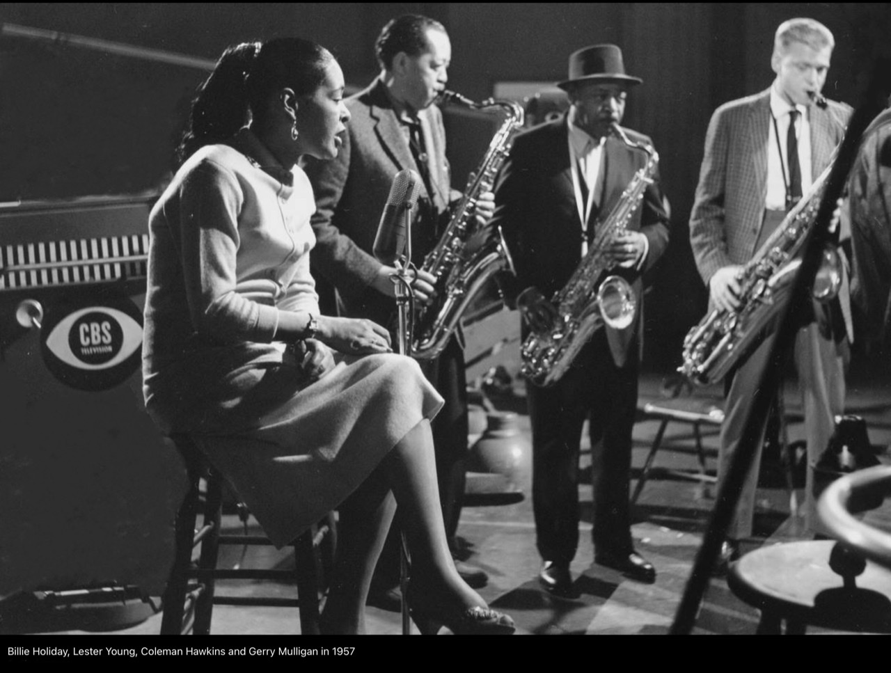 A photograph on the CBS network of the jazz program "The Sound of Surprise" (1957) with Billie Holiday sitting on a stool on far left followed by Lester Young, Coleman Hawkins, and Gerry Mulligan all playing their respective horns while Holiday listens.