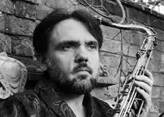 Headshot of Professor James Tartaglia gazing off to right holding saxophone raised up in left hand.