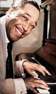 A colorized black and white photograph of Duke Ellington facing right in profile sitting bent over the piano with a big smile turned towards the camera and his hands on the keyboard 🎹.