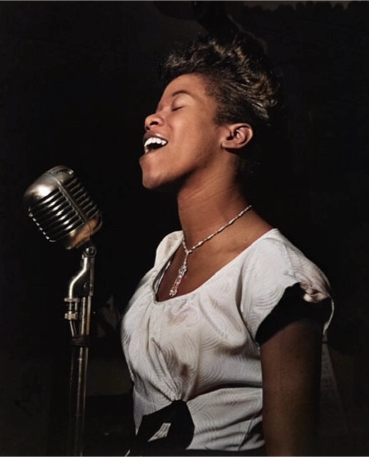 Mirror image of Sarah Vaughn in 1942 singing into a large silver microphone 🎙.
